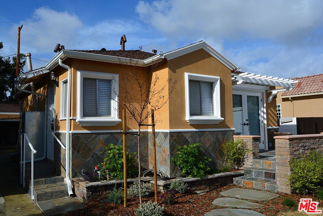 Front elevation of 3565 Wesley St, Culver City: a 1947 stucco duplex with a pergola entry and stone planter walls